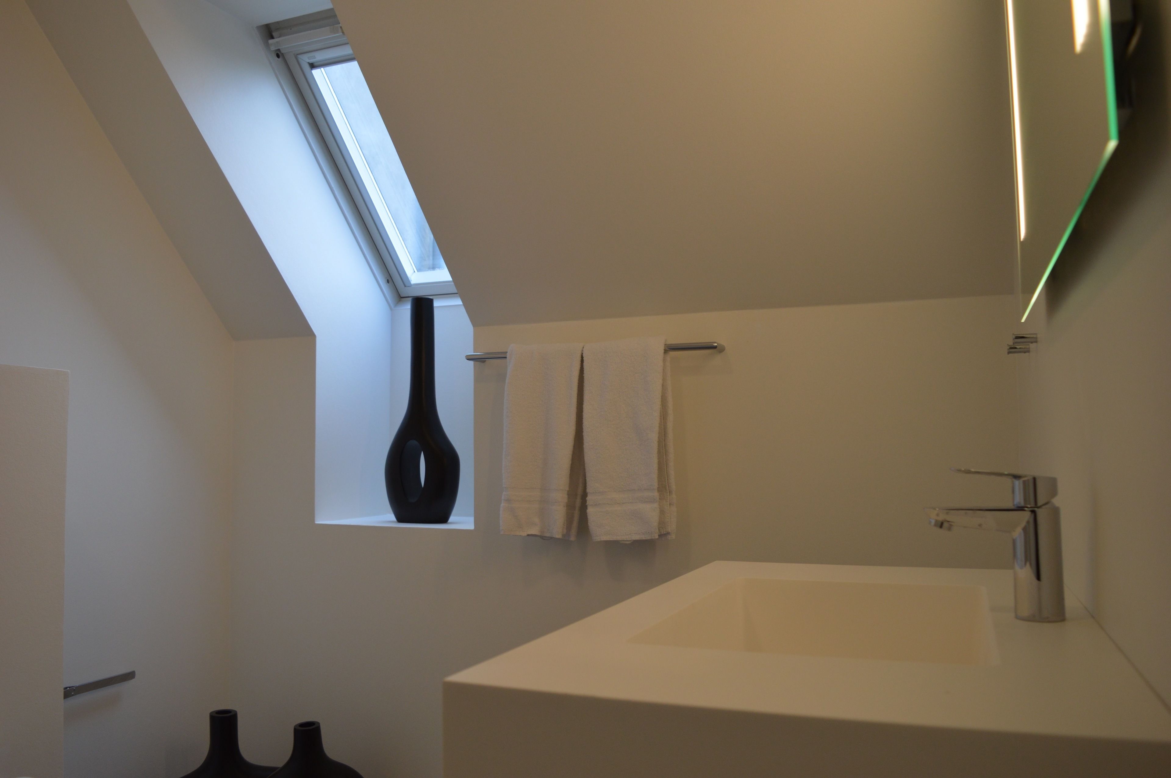 Een moderne badkamer met dakraam, een ruime badkuip en twee zwarte vazen op de vloer.