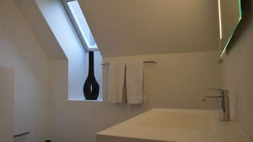 Een moderne badkamer met dakraam, een ruime badkuip en twee zwarte vazen op de vloer.