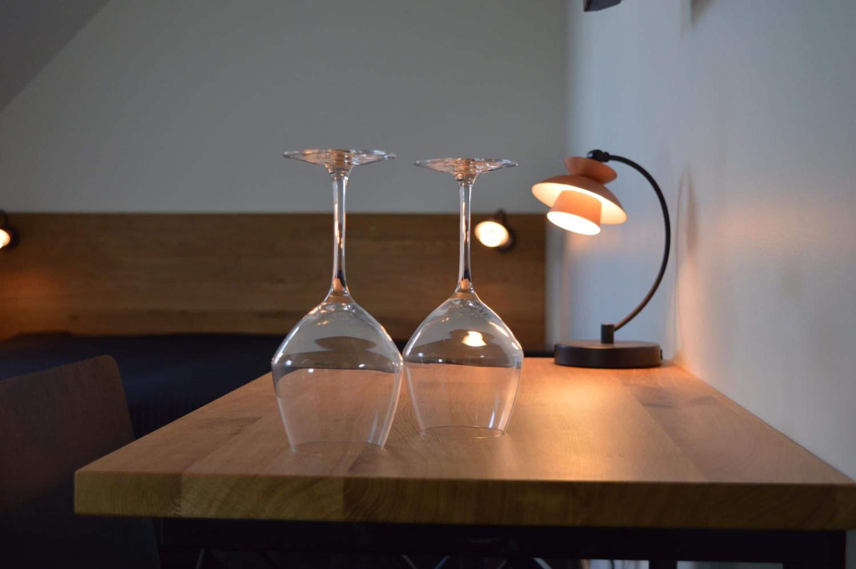 Två eleganta vinglas står på ett träbord, med en lampa i bakgrunden.