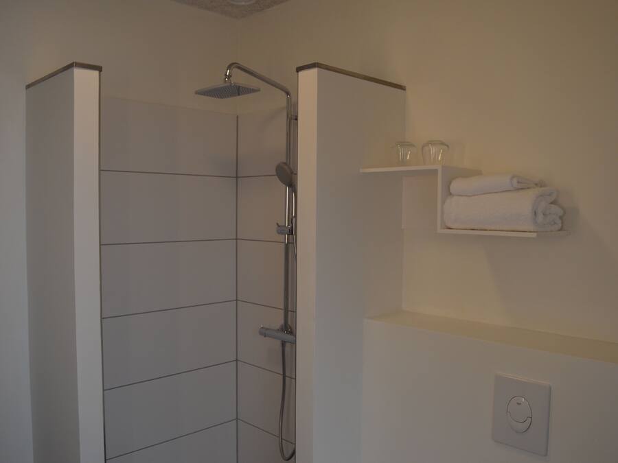 A shower with a handheld showerhead and a wall-mounted faucet. There is a towel rack with folded towels above it.