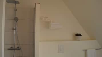 Een badkamer met een douche, handdoekhouder, een plank met handdoeken en een potplant.