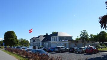 En parkeringsplads med flere biler, en bygning med et flag og en klar blå himmel.