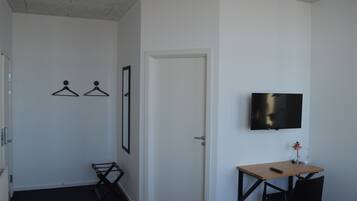 Una habitación con cama, escritorio con silla, televisor montado en la pared y una puerta.
