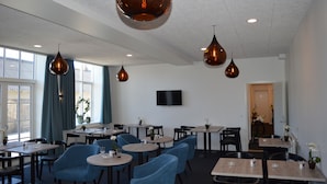 A modern restaurant with round tables, blue chairs, and pendant lighting. - Femhøj (Jægerspris)