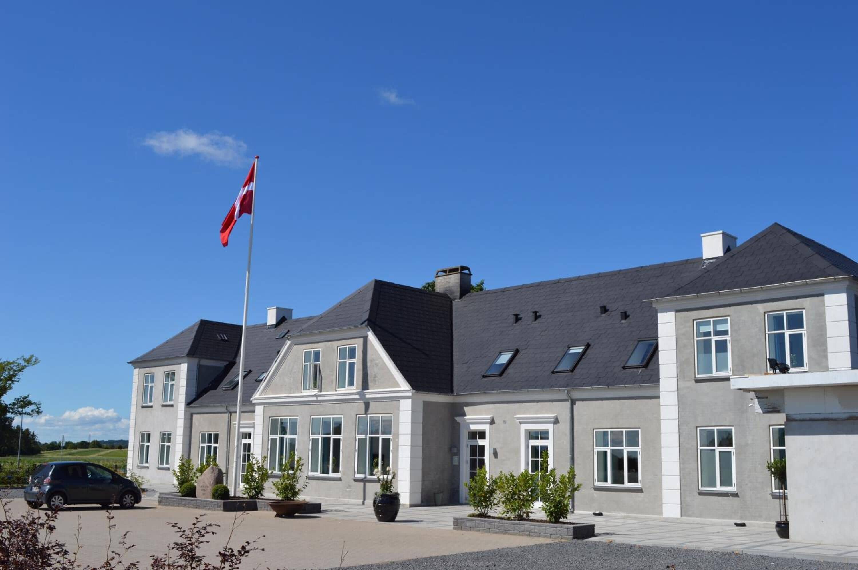 En toetages bygning med en grå facade, flere vinduer og et flagstang med flag.