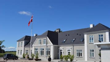 En toetages bygning med en grå facade, flere vinduer og et flagstang med flag.