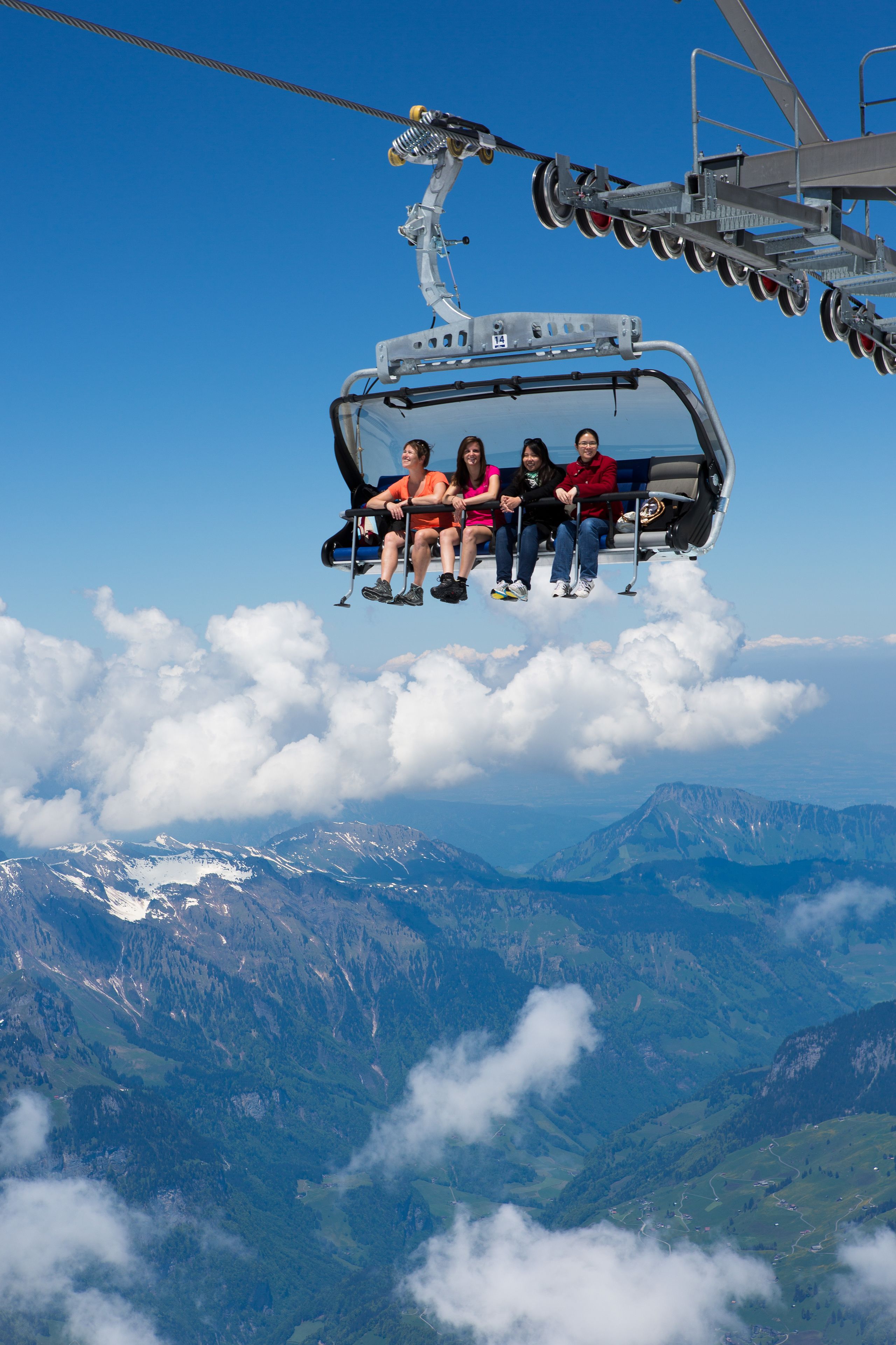 Eine Seilbahn mit Fahrgästen fliegt über Wolken und Berge.