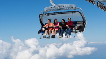Eine Seilbahn mit Fahrgästen fliegt über Wolken und Berge.