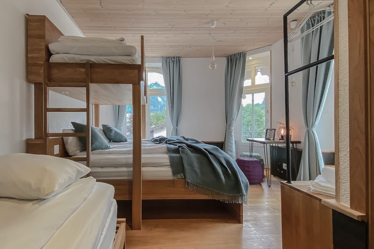 Habitación con literas, un escritorio y una silla, una ventana con cortinas y un cuadro en la pared.