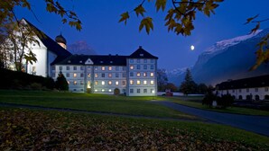 A large, multi-story building with a prominent tower and a well-lit facade. - GRAND your home with common kitchens with self check-in (Engelberg)