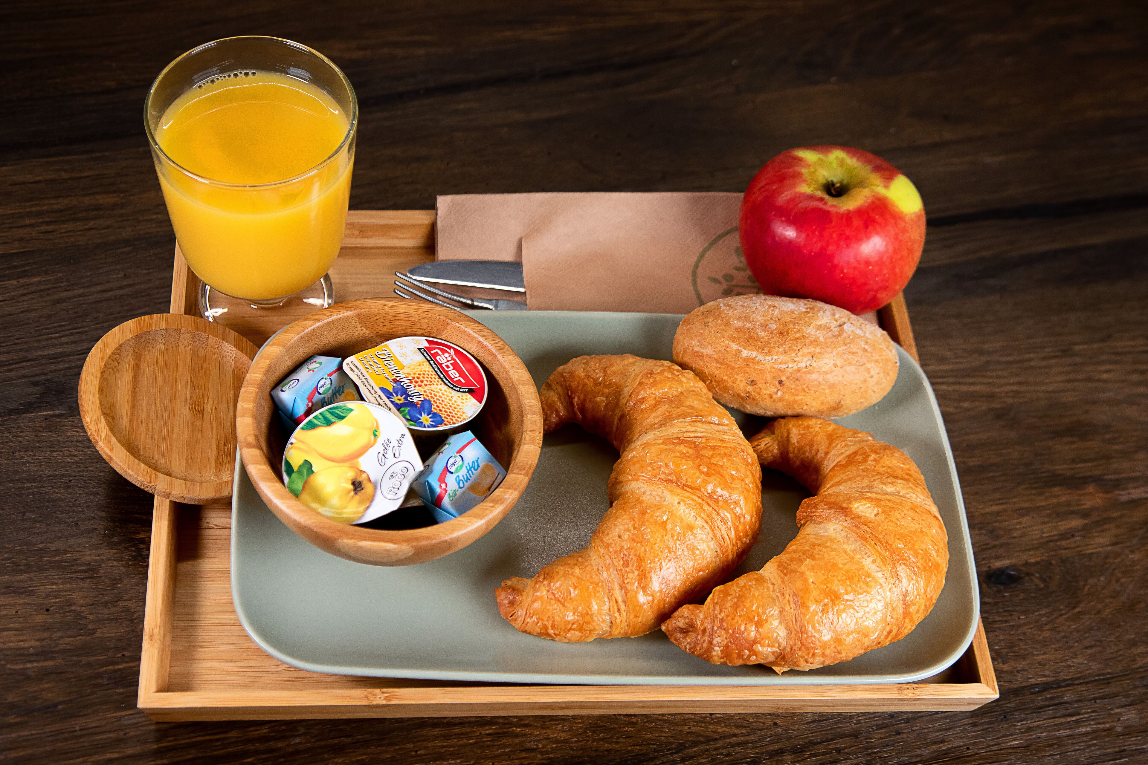 Bandeja de desayuno con croissants, una manzana, jugo y un tazón de cereal.