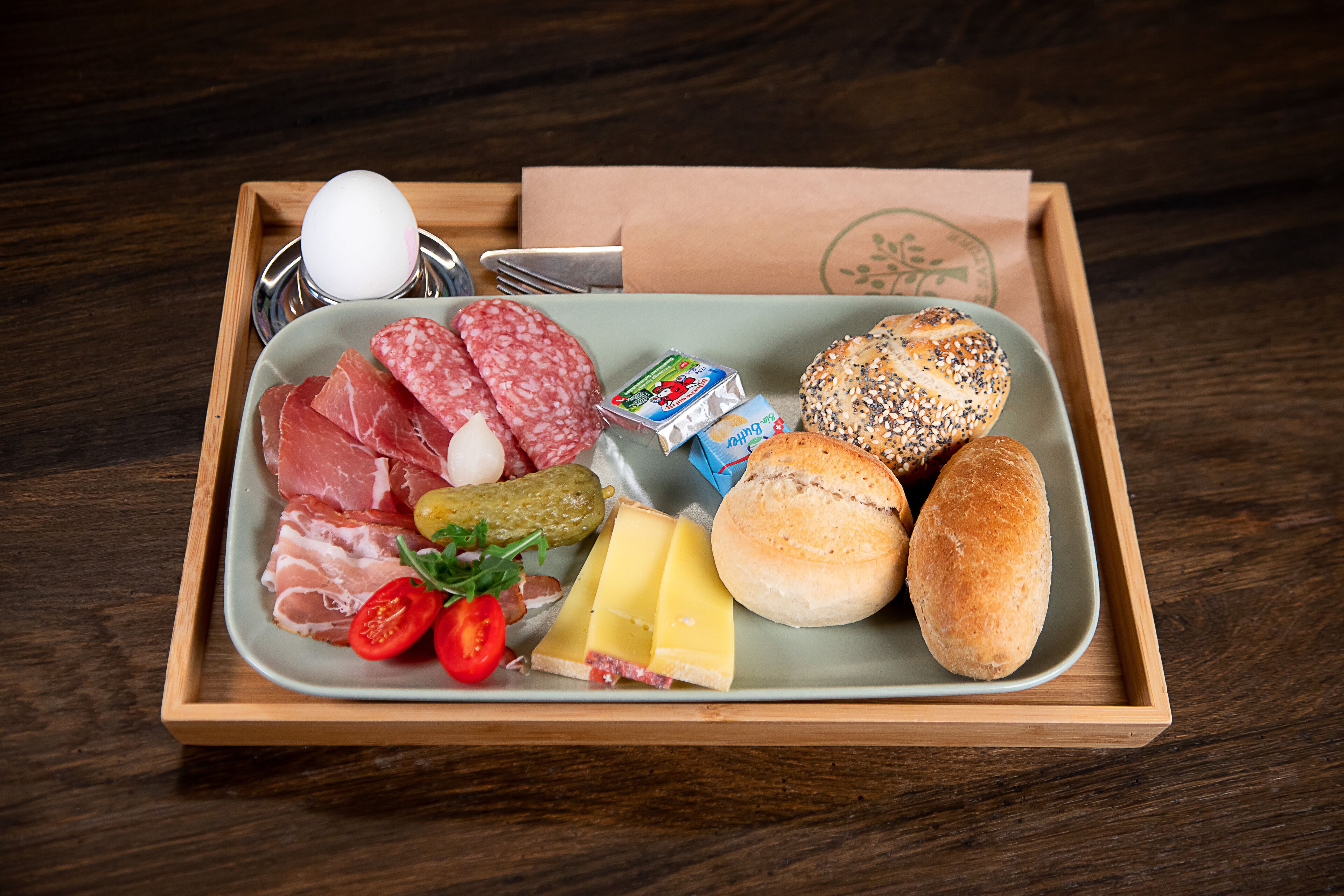 A wooden tray with a variety of food items including meats, cheese, bread, and a boiled egg.