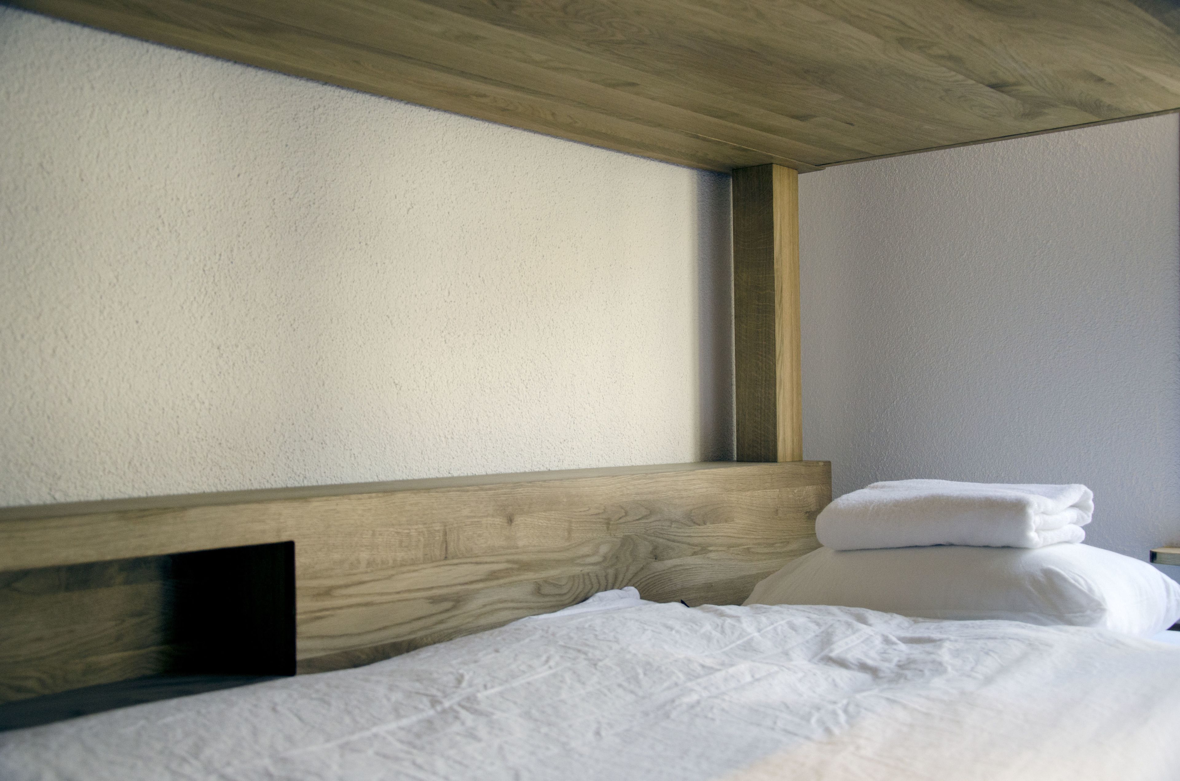 A neatly made bed with white linens and a wooden headboard in a room with light-colored walls.
