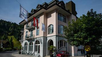 A two-story building with a balcony, a red car parked in front, and a flag.