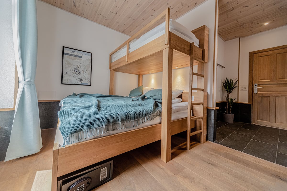 Una cama litera con escalera, un escritorio pequeño y una planta en maceta en una habitación con suelo y techo de madera.