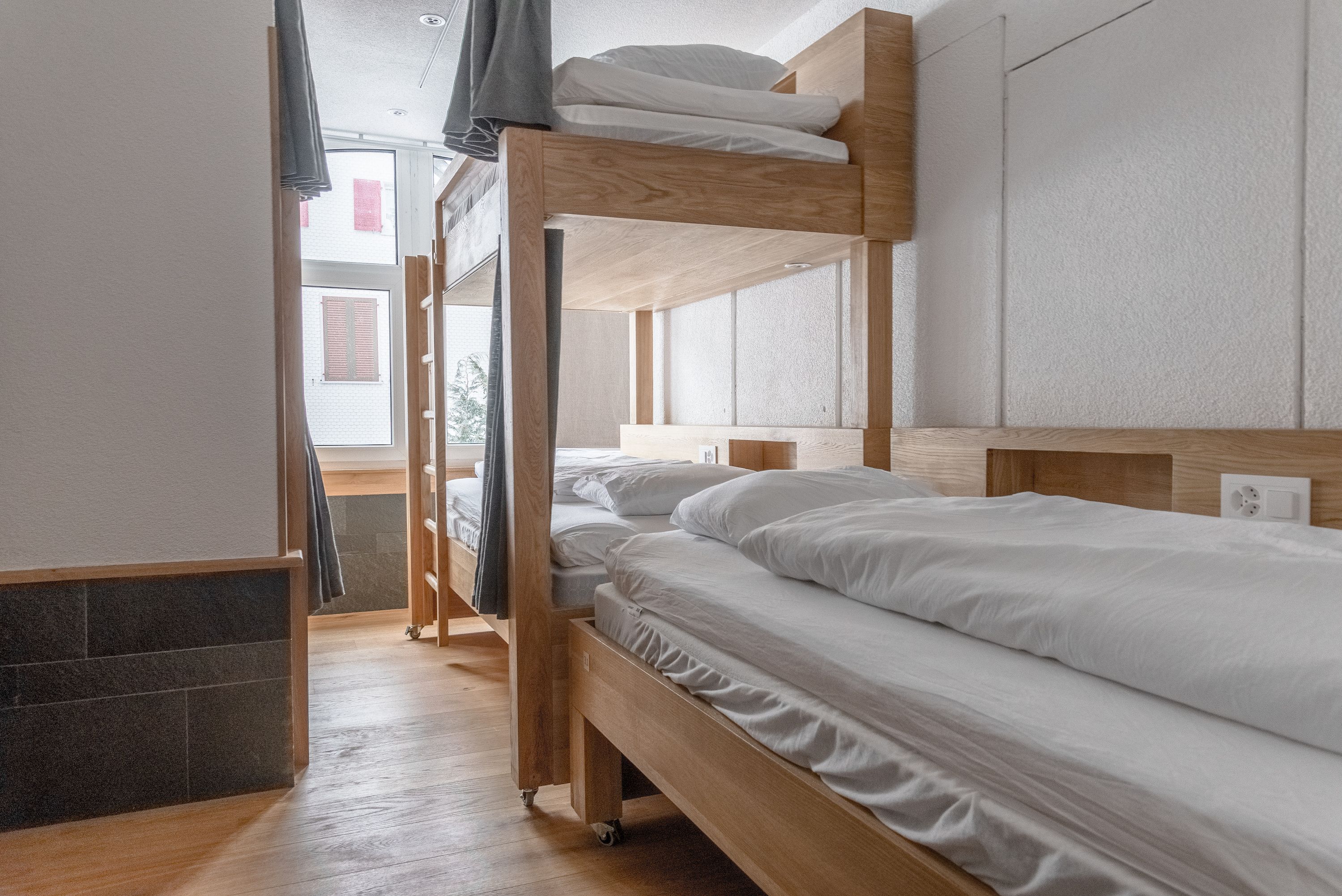 A bunk bed room with a wooden headboard, a small window, and a tiled floor.