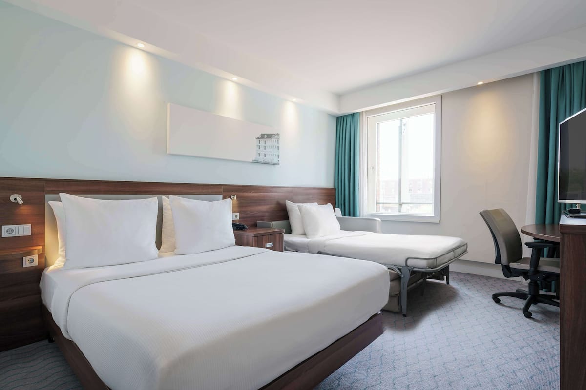 A hotel room with two beds, a desk with a chair, a television, and a window with curtains.