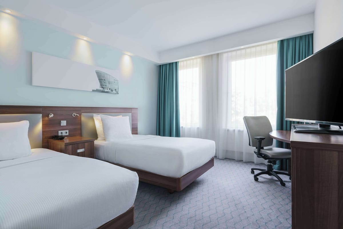 A hotel room with two beds, a desk, a chair, a TV, and a painting on the wall.