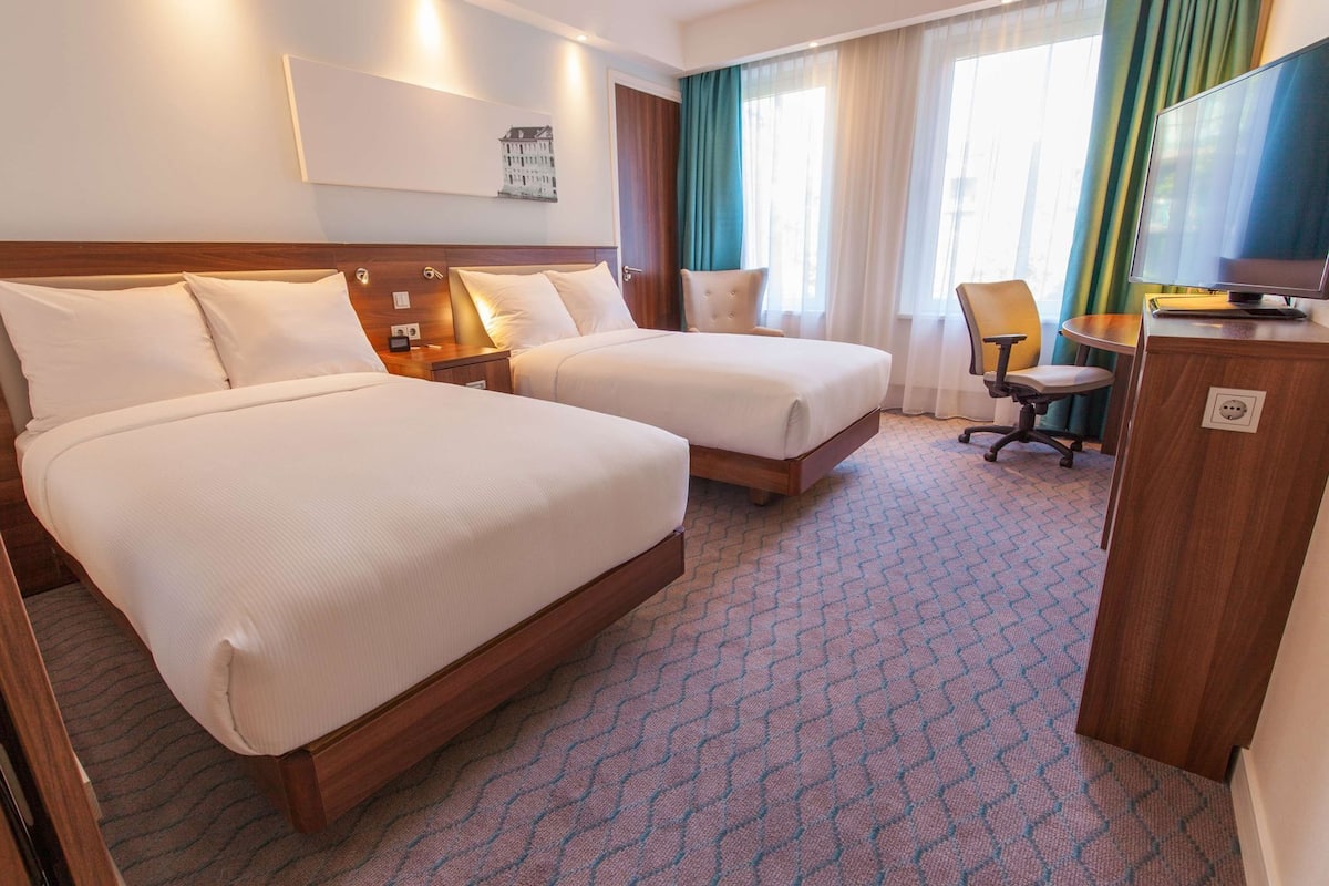 A hotel room with two beds, a desk, a chair, and a television.