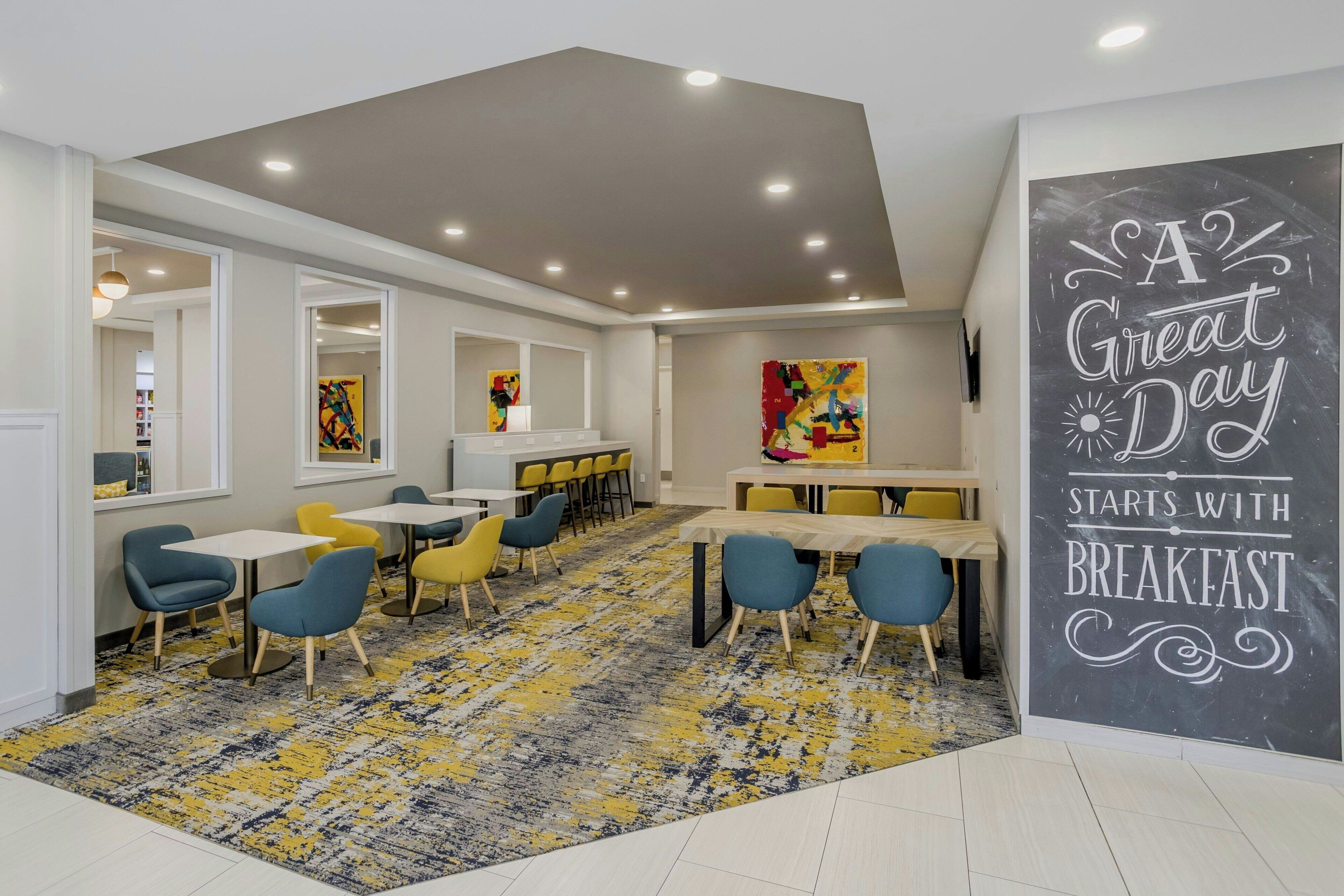 Un comedor moderno con alfombra estampada, varias mesas y sillas, y obras de arte en las paredes.