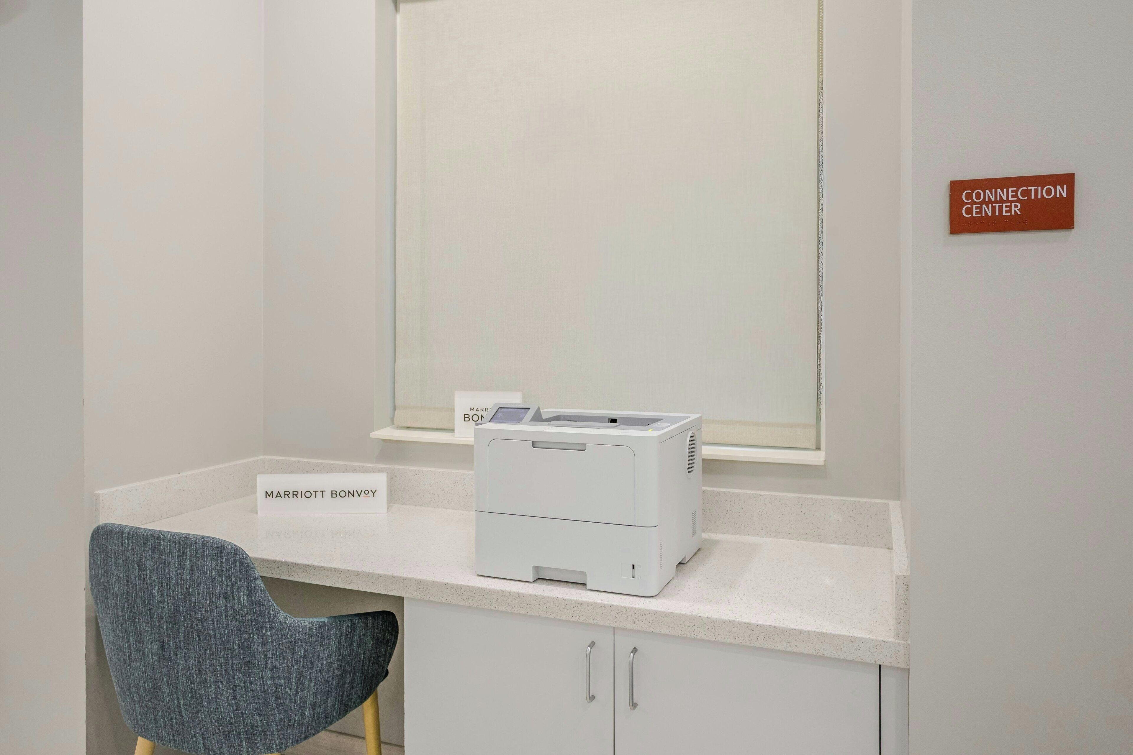 Un mostrador de recepción de hotel con una computadora, un cartel que dice 'MARRIOTT BONVOY' y un letrero de 'CENTRO DE CONEXIONES' en la pared.