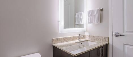 A bathroom with a toilet, a sink with a granite countertop, dark cabinets, and a mirror above the sink.