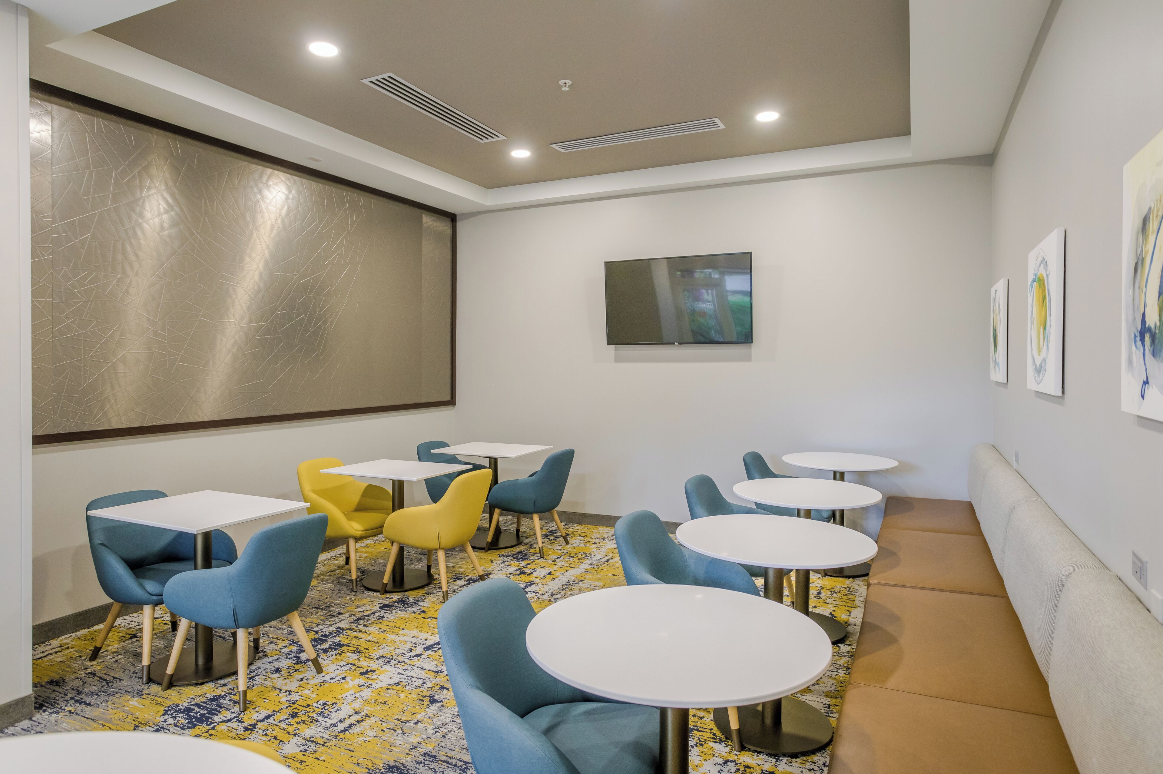 A conference room with a large projection screen, multiple tables and chairs, and artwork on the walls.