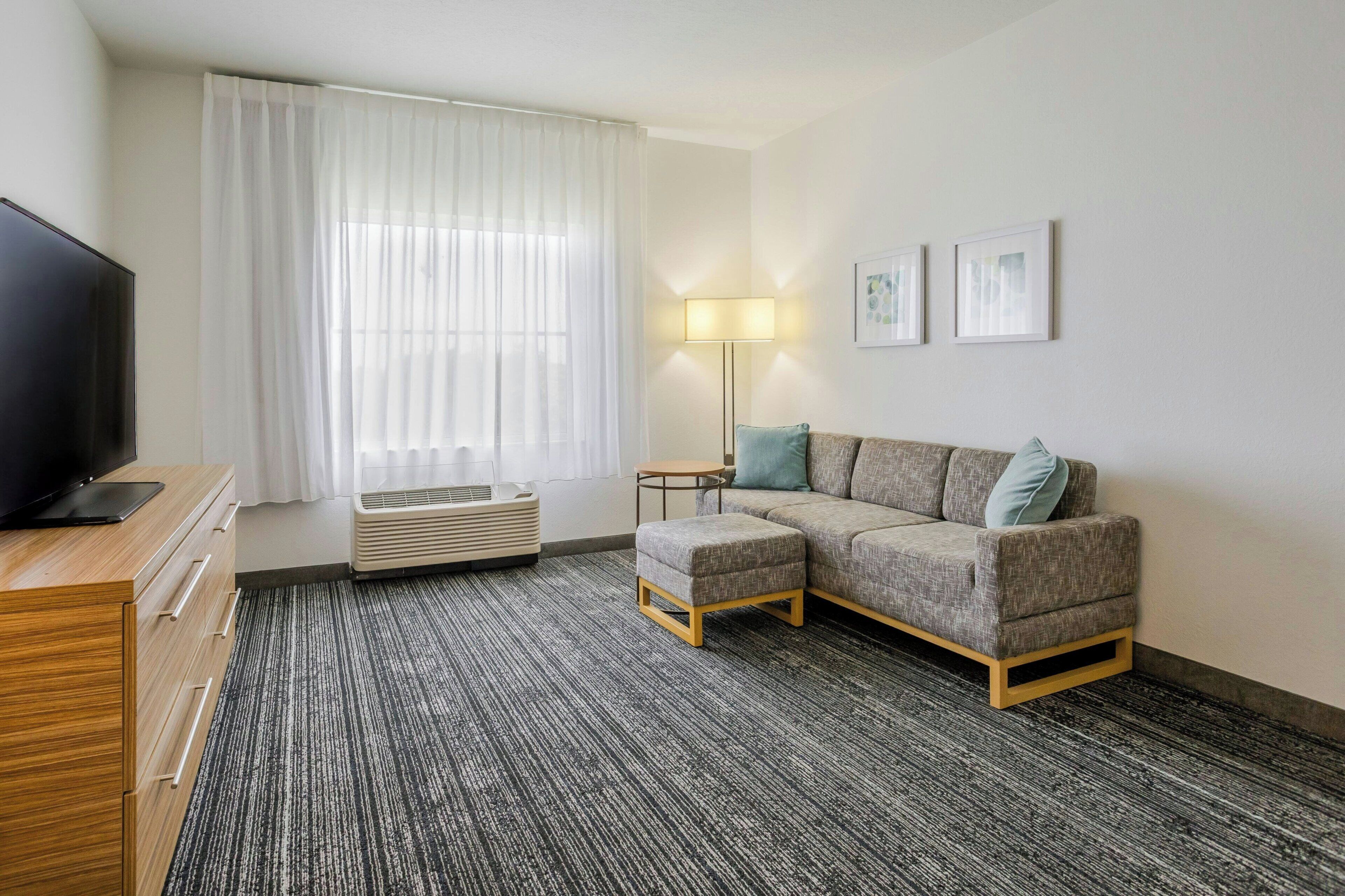 A hotel room with a sofa, a TV, a lamp, and a window with curtains.