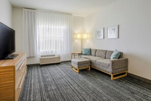 A hotel room with a sofa, a TV, a lamp, and a window with curtains.