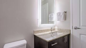 Un baño con inodoro, un lavabo con encimera de granito, armarios oscuros y un espejo sobre el lavabo.