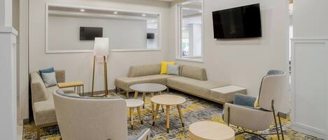 A modern living room with a sofa, armchairs, a coffee table, and a TV mounted on the wall.