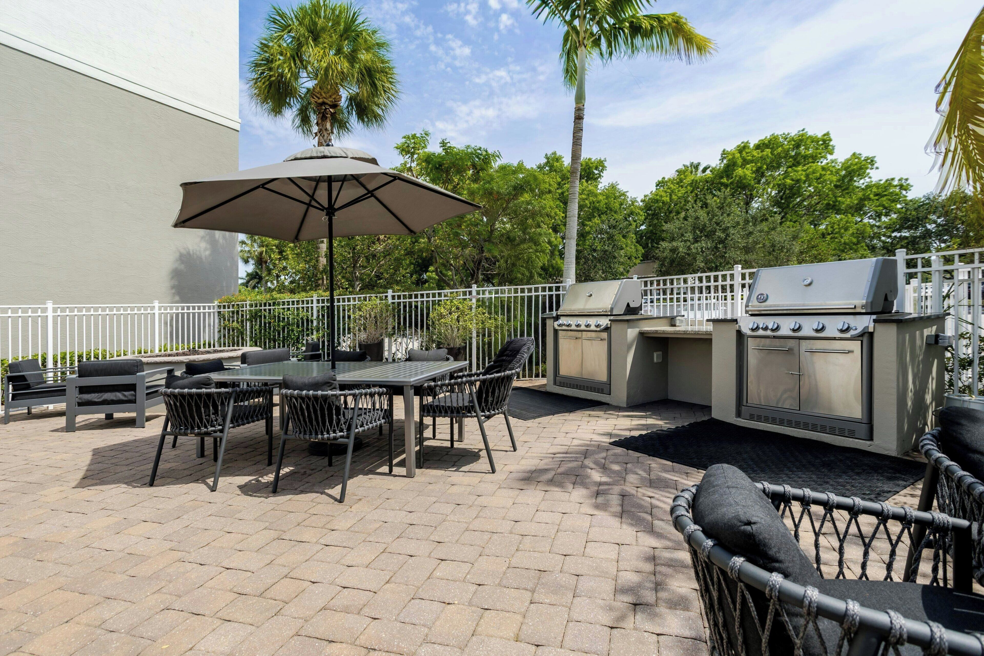 An outdoor patio with a dining table, chairs, an umbrella, and a barbecue grill.