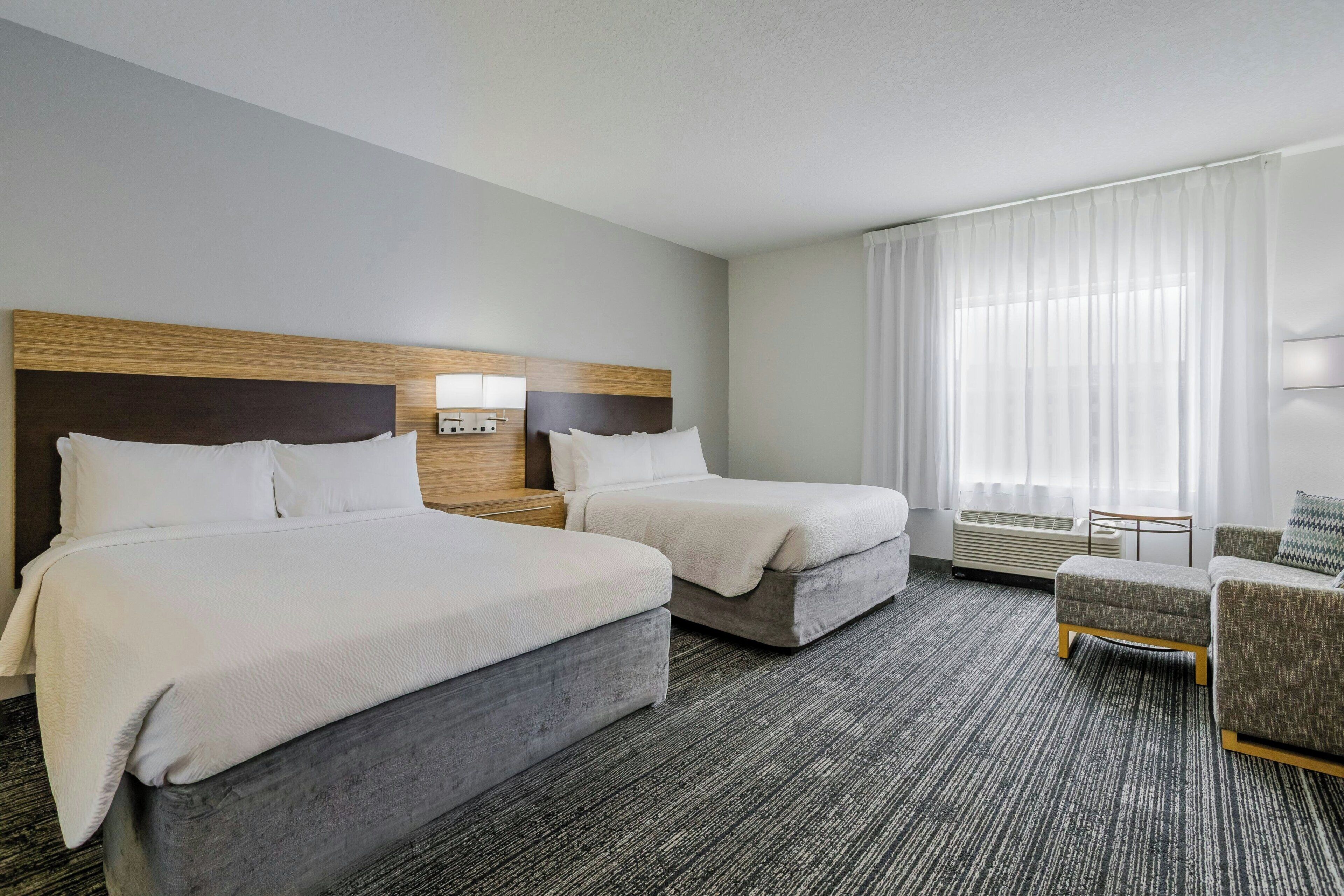 A hotel room with two beds, a sitting area, and a large window with curtains.