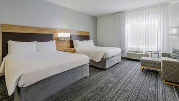 A hotel room with two beds, a sitting area, and a large window with curtains.