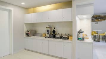 A modern kitchen with white cabinets, a built-in oven, a coffee machine, and a small dining area with yellow chairs.