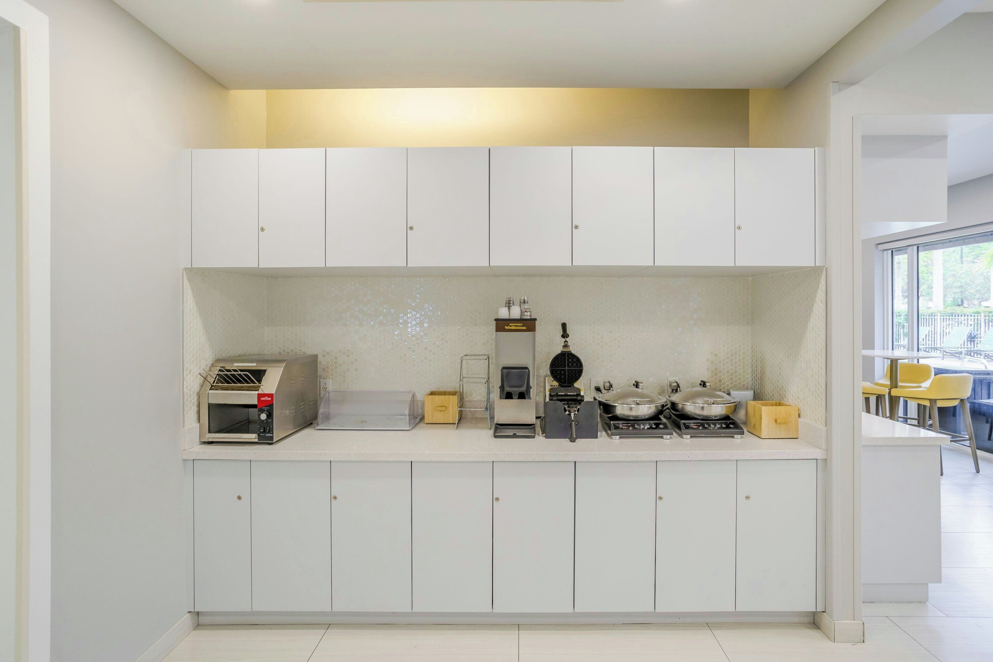 A modern kitchen with white cabinets, a built-in waffle maker, a coffee machine, and a stove.