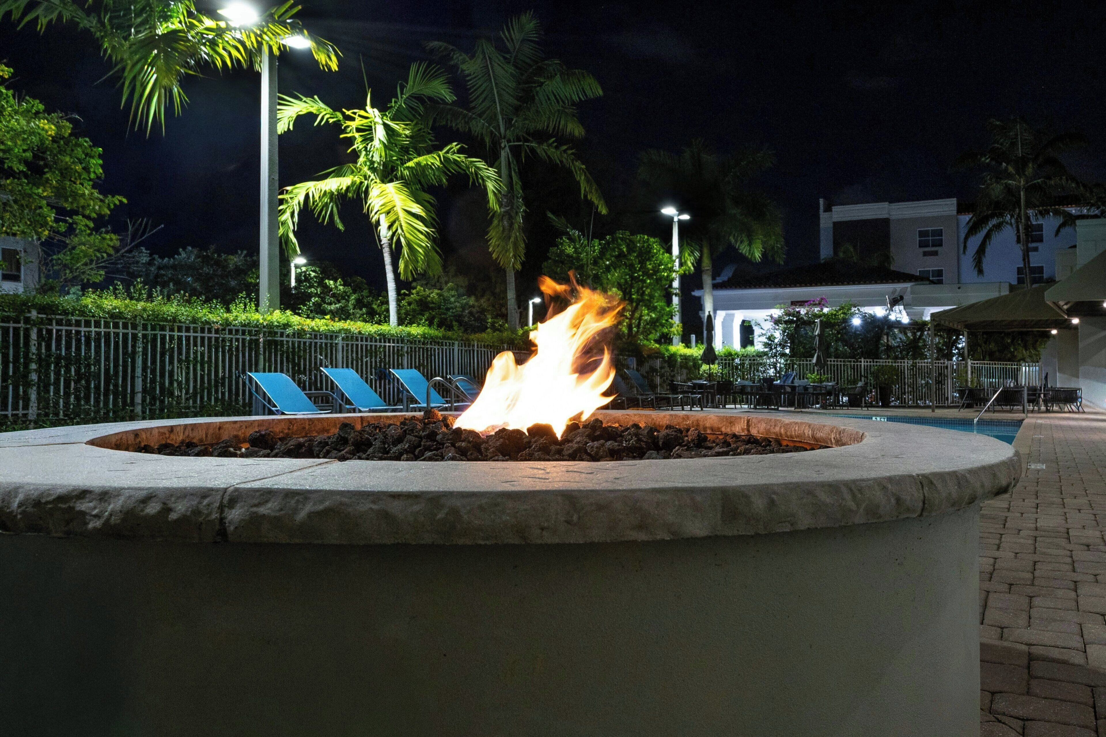 A night scene with a fire feature in a circular stone planter surrounded by a metal fence.