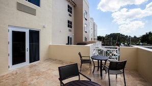 A balcony with outdoor seating, a sliding door, and a building with multiple windows and balconies. - TownePlace Suites By Marriott Boynton Beach (Boynton Beach)
