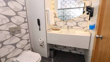 A bathroom with a toilet, sink, mirror, and a trash bin.