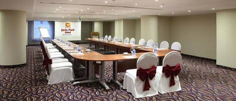 A conference room with a long table, white chairs with red bows, and a carpeted floor.