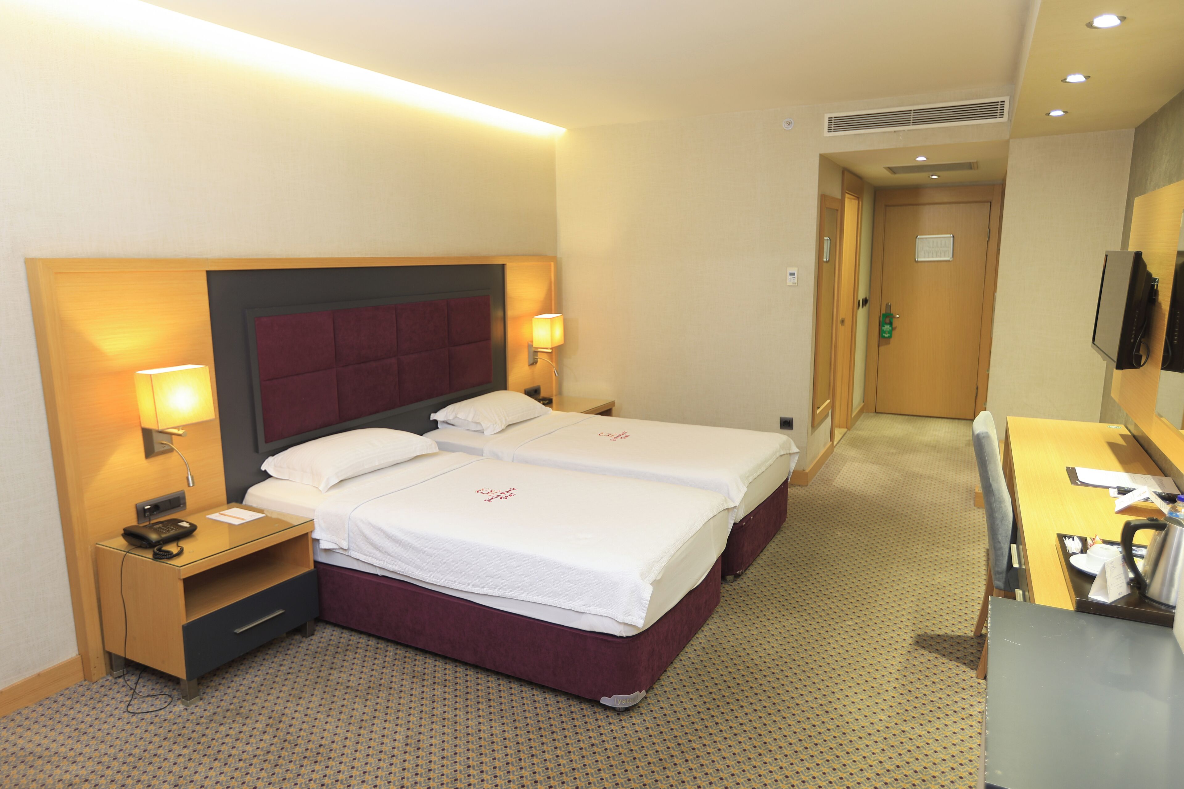 A hotel room with two beds, a desk, a chair, a TV, and a bathroom door.