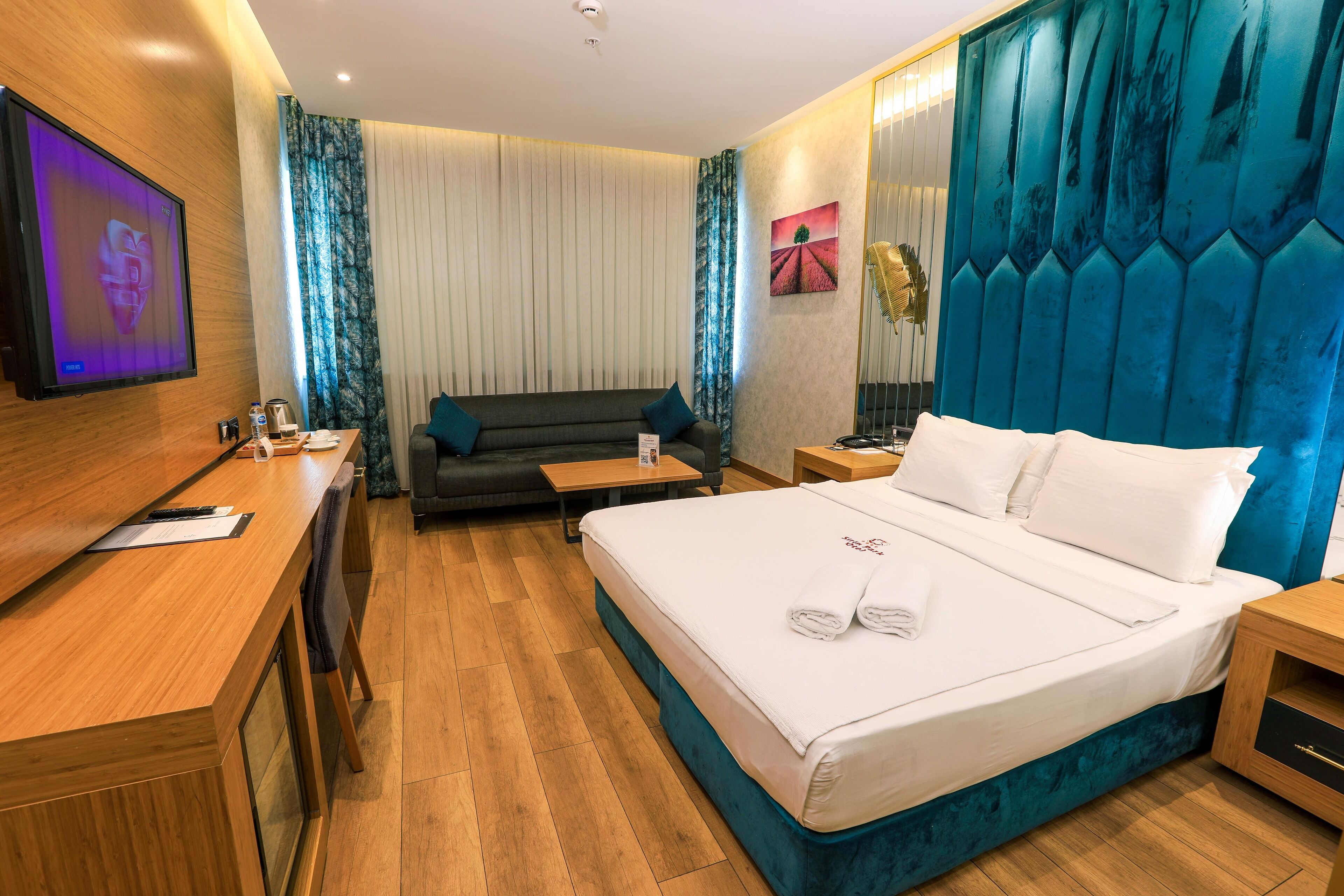 A modern hotel room with a large bed, a sofa, a desk, and a TV.
