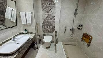 A modern bathroom with a granite countertop sink, a toilet, a shower with a handheld showerhead, and a glass-enclosed shower stall.