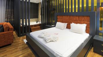 A modern hotel room with a large bed, a wooden floor, a bathroom with a bathtub, and a seating area with a sofa.