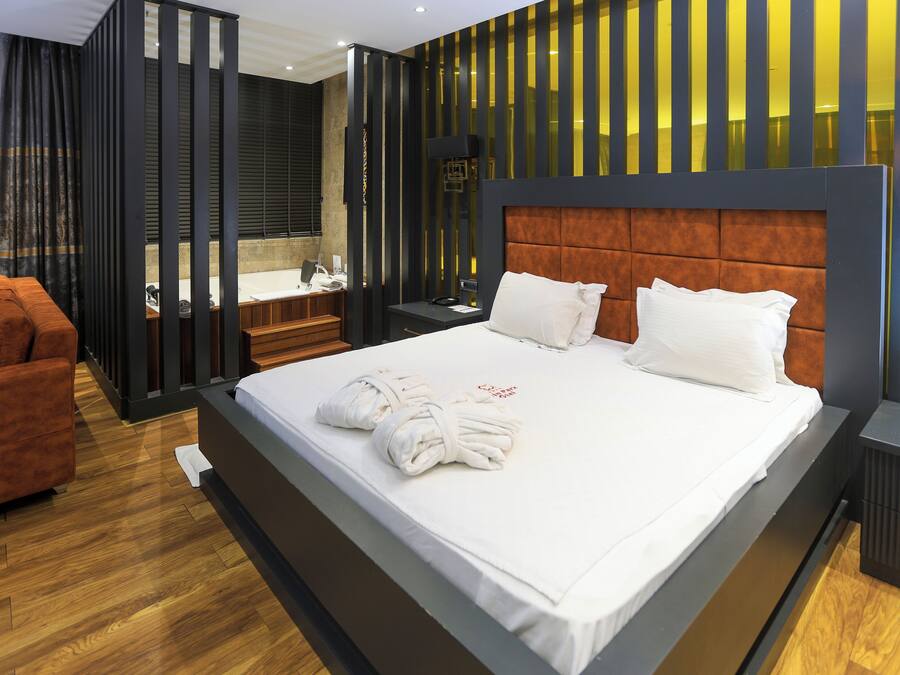 A modern hotel room with a large bed, a wooden floor, a bathroom with a bathtub, and a seating area with a sofa.