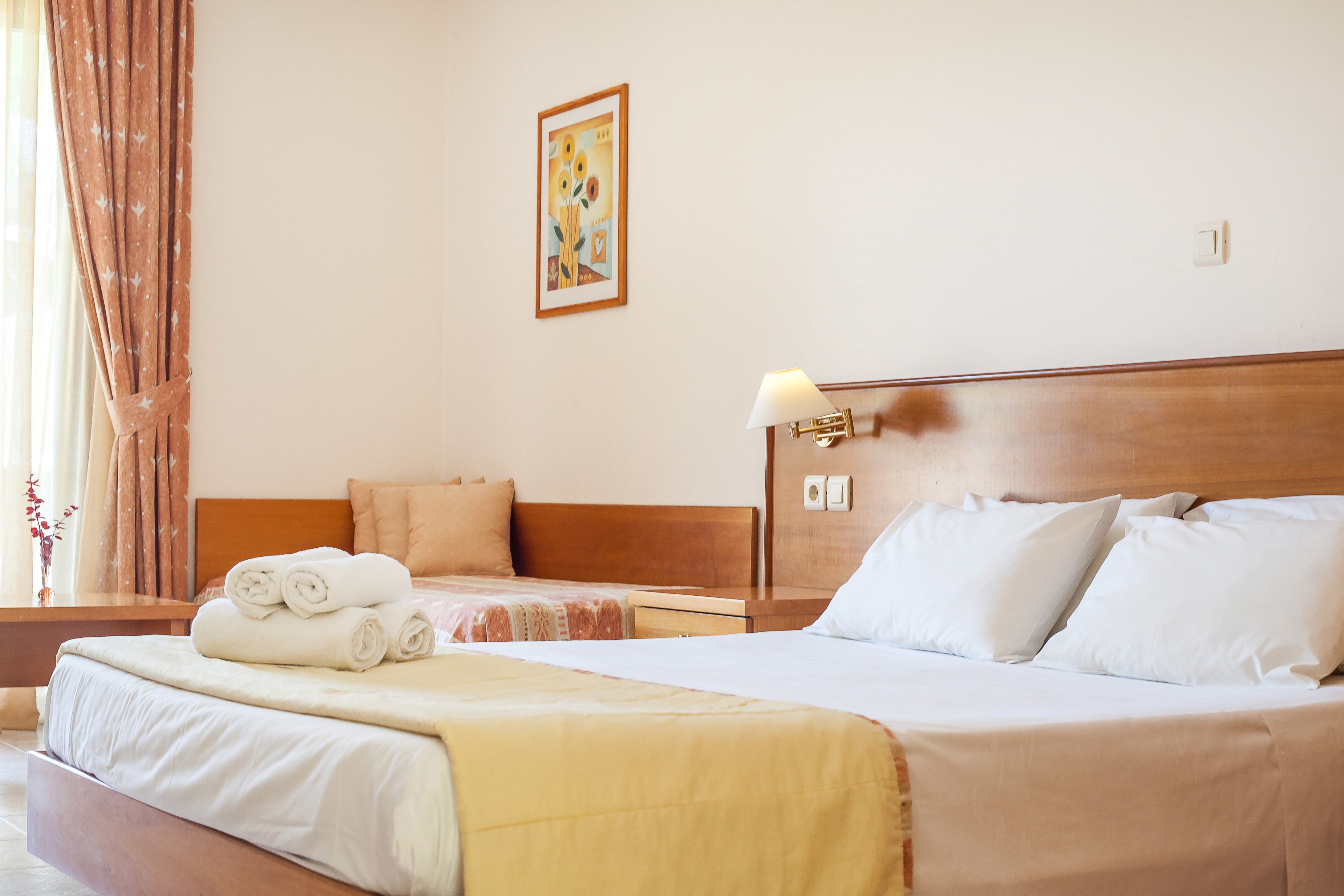 Habitación de hotel con una cama grande, una cama más pequeña, una mesita de noche, una lámpara y un cuadro en la pared.
