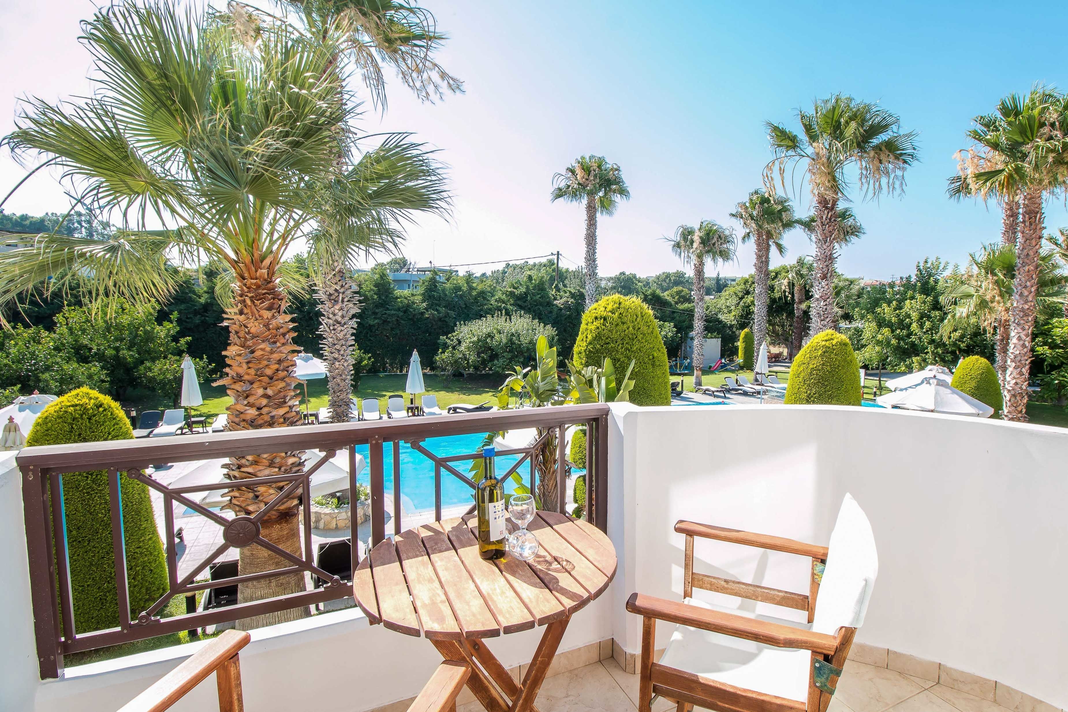 A balcony with a wooden table and chairs, overlooking a swimming pool and lush greenery.