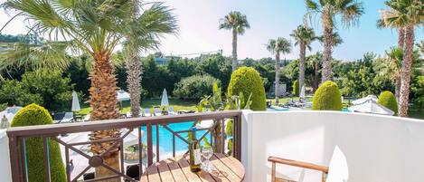 Un balcon avec une table et des chaises en bois, donnant sur une piscine et une végétation luxuriante.