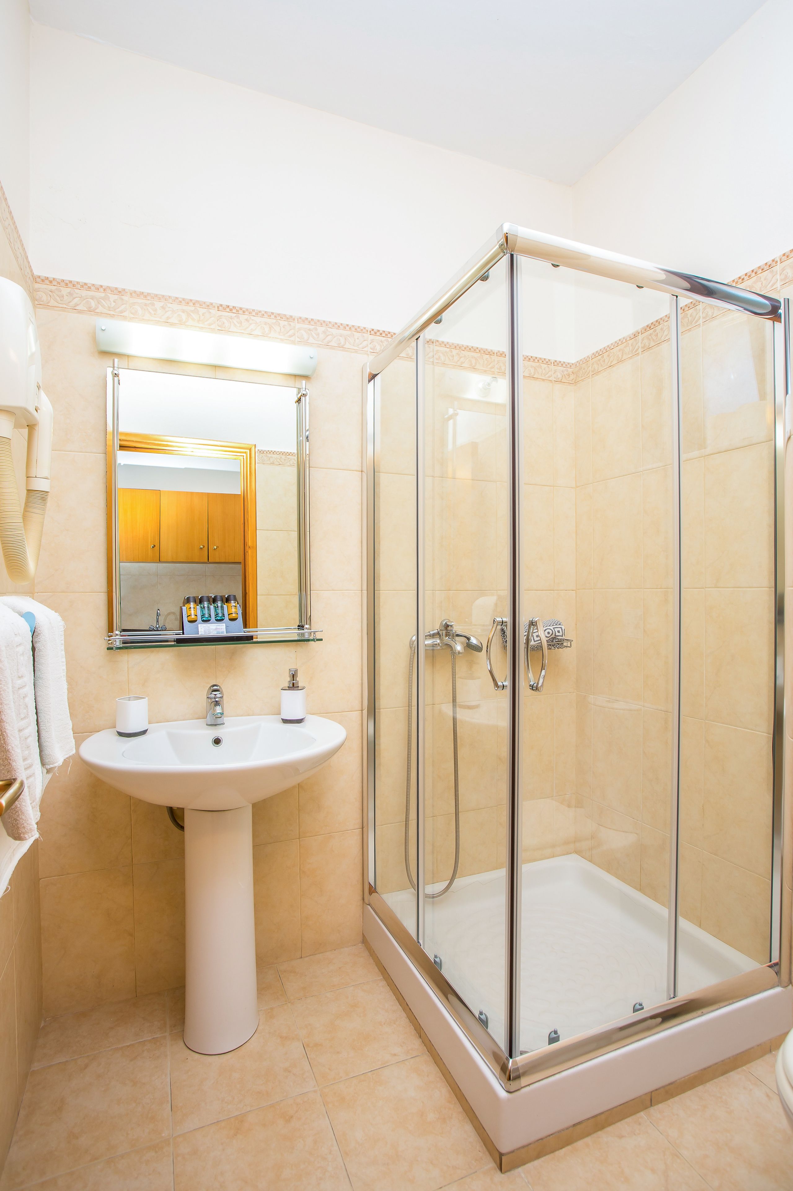 A bathroom with a glass-enclosed shower, a pedestal sink, and a mirror above the sink.