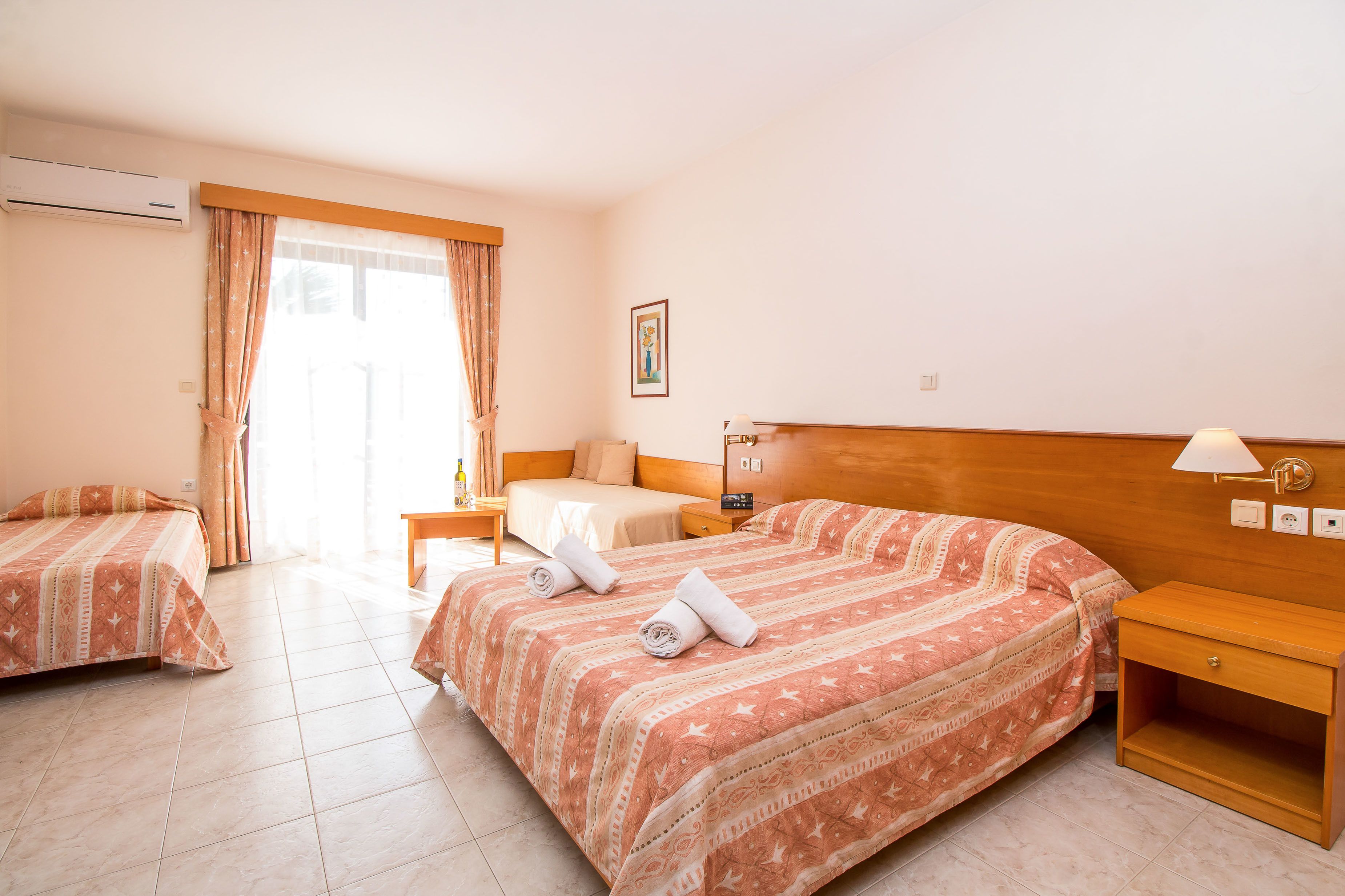Habitació d'hotel amb dos llits, un capçal de fusta, una tauleta de nit, una làmpada i un quadre a la paret.